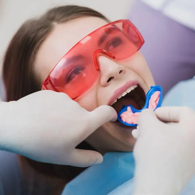 Child wearing pink glasses receiving dental examination with mouth guard in dentist's office.