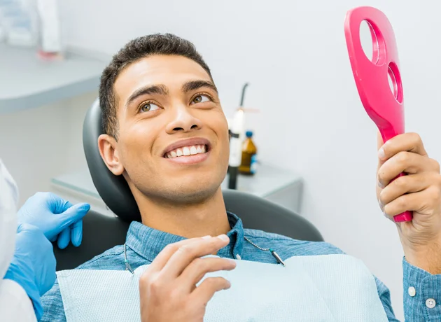 Young man wearing blue gloves examining pink toothbrush in dental office setting.