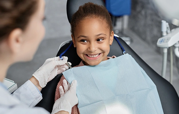 Young girl smiling in dental chair during examination with dentist in clinical setting.