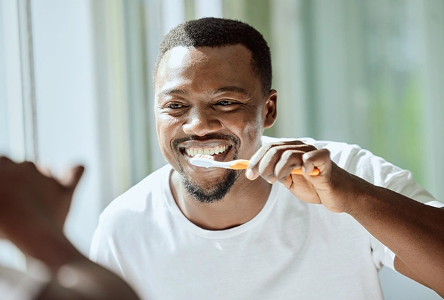 Smiling man brushing teeth in bright bathroom, promoting dental hygiene and oral care.