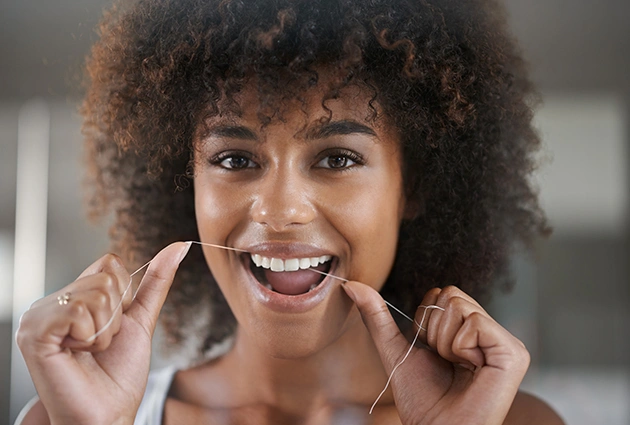 Smiling woman with curly hair touching her face in a bright dental office setting.