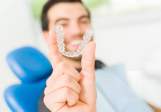 Patient holding clear dental aligners in dentist's office with dental professional in background